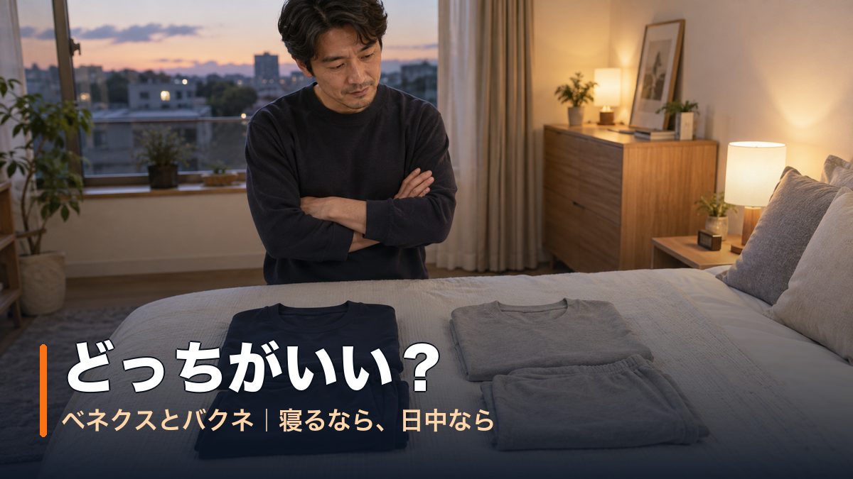 夕方の寝室でベッドに並べた紺と灰色の2着を腕を組んで見比べる男性｜ベネクスとバクネどっちがいい